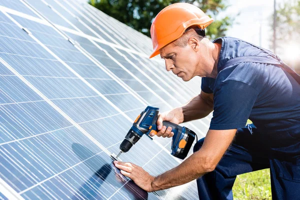 Handsome engineer in t-shirt and orange hardhat using drill — Stock Photo