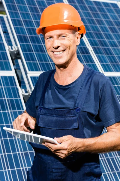 Engenheiro bonito em t-shirt e hardhat laranja sorrindo e segurando tablet digital — Fotografia de Stock