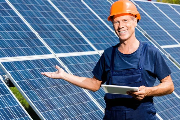 Handsome engineer in t-shirt and orange hardhat smiling and holding digital tablet — Stock Photo