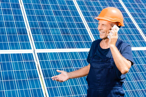 Bellissimo ingegnere in t-shirt e hardhat arancione sorridente e parlante su smartphone — Foto stock