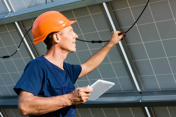 Engenheiro bonito em t-shirt e hardhat laranja sorrindo e segurando tablet digital — Fotografia de Stock