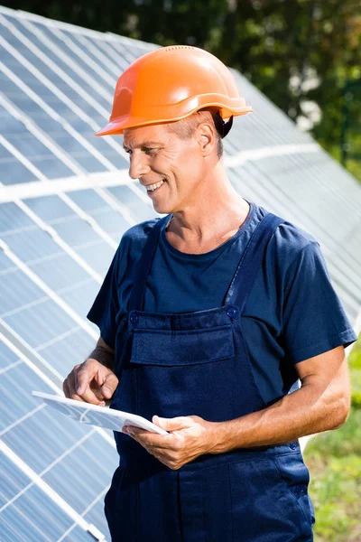 Bell'ingegnere in t-shirt e hardhat arancione sorridente e in possesso di tablet digitale — Foto stock