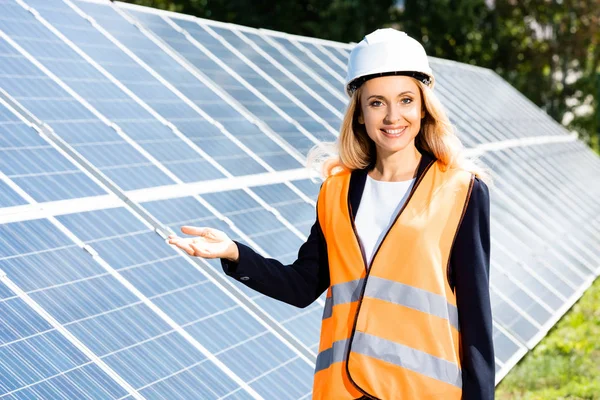 Mujer de negocios en chaleco de seguridad y hardhat sonriendo y mirando a la cámara - foto de stock