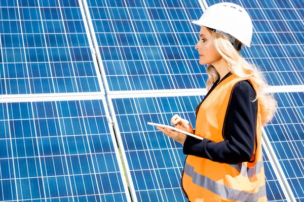 Vista laterale della donna d'affari in giubbotto di sicurezza e hardhat utilizzando tablet digitale — Foto stock