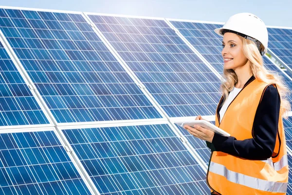 Mujer de negocios en chaleco de seguridad y hardhat sonriendo y utilizando tableta digital - foto de stock