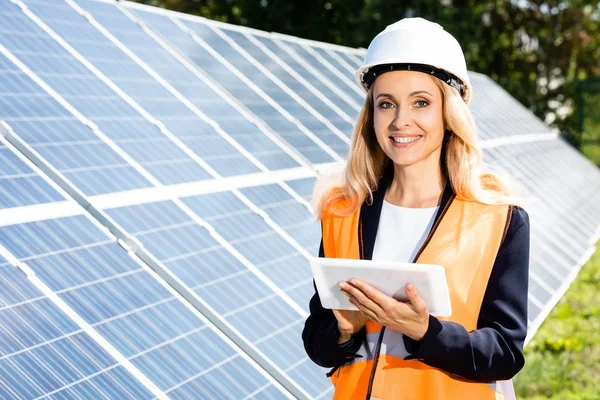 Empresária em colete de segurança e hardhat sorrindo e usando tablet digital — Fotografia de Stock