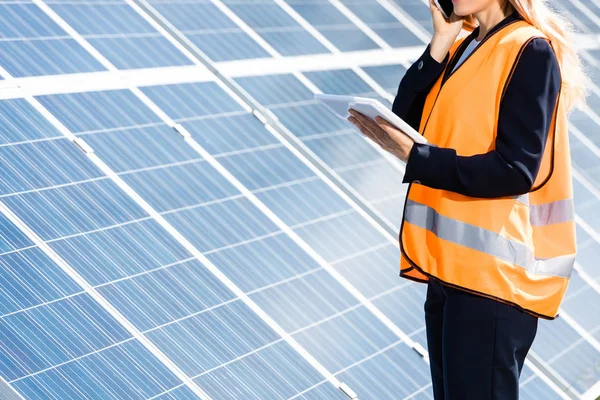 Cropped view of businesswoman in safety vest talking on smartphone and holding digital tablet — Stock Photo