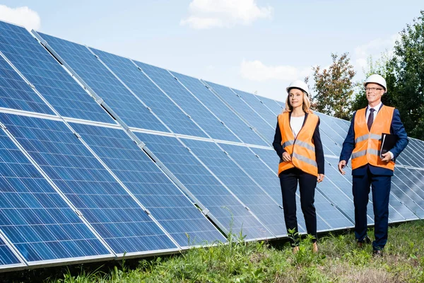 Hombre de negocios guapo y atractiva mujer de negocios caminando cerca de baterías de energía solar - foto de stock