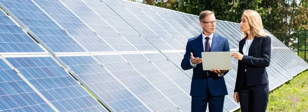 Panoramaaufnahme eines gut aussehenden Geschäftsmannes und einer attraktiven Geschäftsfrau, die mit Laptop redet und hält — Stockfoto