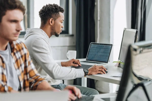 Enfoque selectivo de dos programadores multiculturales que trabajan juntos en la oficina - foto de stock