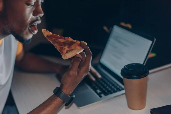 Jovem programador afro-americano comendo pizza enquanto está sentado no local de trabalho — Fotografia de Stock