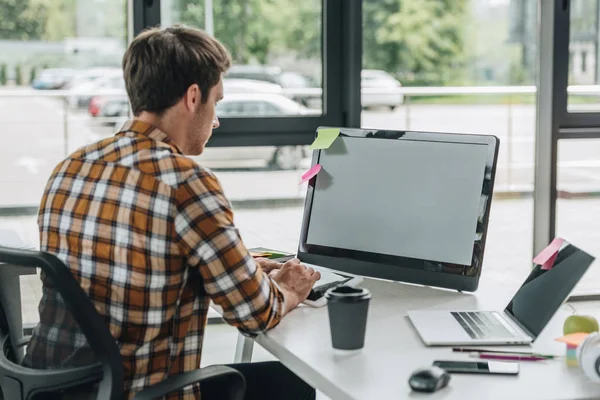 Vue arrière du jeune programmeur travaillant sur ordinateur assis sur le lieu de travail près de la fenêtre — Photo de stock