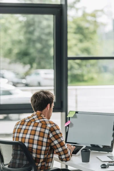 Vista trasera del joven programador sentado en el lugar de trabajo cerca de la ventana - foto de stock