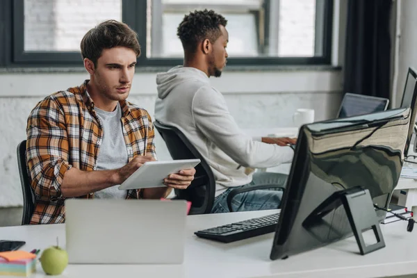 Junger Programmierer benutzt digitales Tablet, während er in der Nähe eines amerikanischen Kollegen sitzt — Stockfoto