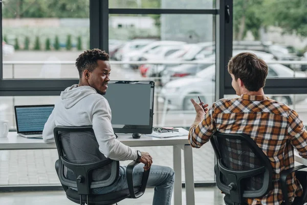 Vue arrière du jeune programmeur parlant à un collègue afro-américain au bureau — Photo de stock