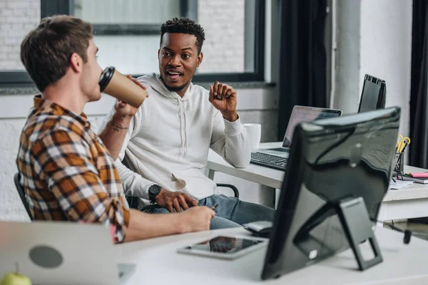 Deux jeunes programmeurs multiculturels parlent en étant assis ensemble au bureau — Photo de stock