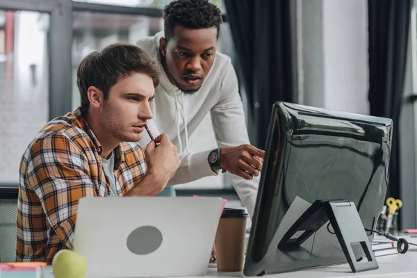 Afrikanischer amerikanischer Programmierer zeigt in der Nähe eines ernsthaften Kollegen auf Computermonitor — Stockfoto