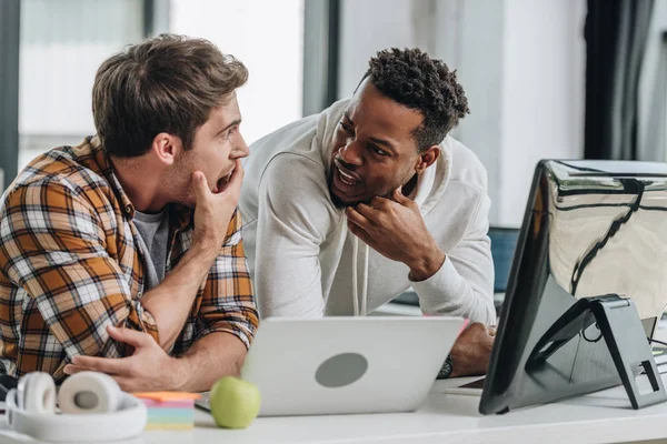 Dois programadores multiculturais chocados olhando um para o outro enquanto trabalham no escritório juntos — Fotografia de Stock