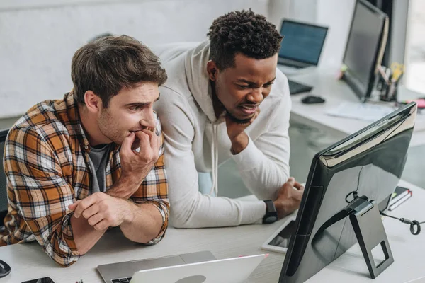 Two worried multicultural programmers looking at laptop in office — Stock Photo