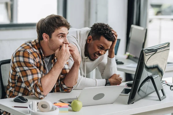 Dois programadores multiculturais chocados olhando para laptop no escritório — Fotografia de Stock