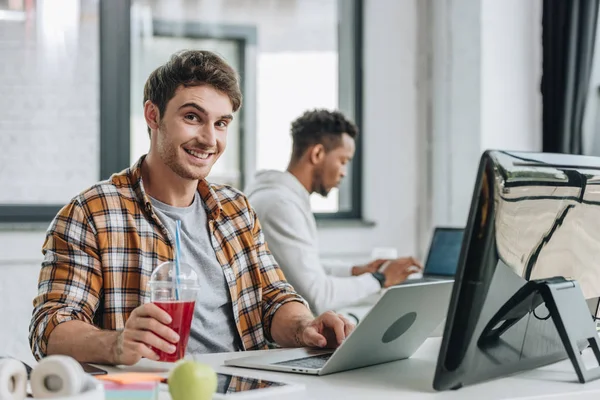 Programador alegre olhando para a câmera enquanto sentado perto de colega afro-americano — Fotografia de Stock