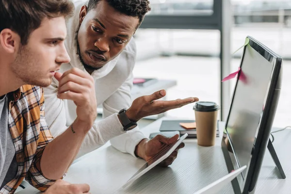 Serious african american programmer pointing at computer monitor near colleague — Stock Photo