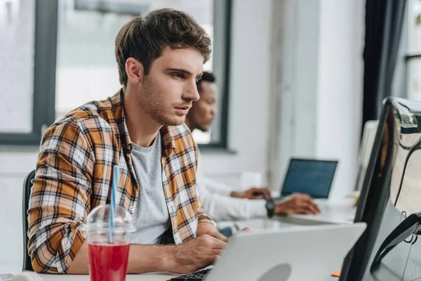 Selective focus of attentive programmer working in office near african american colleague — Stock Photo