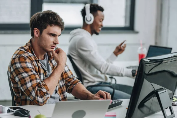 Selective focus of thoughtful programmer working near african american colleague in office — Stock Photo