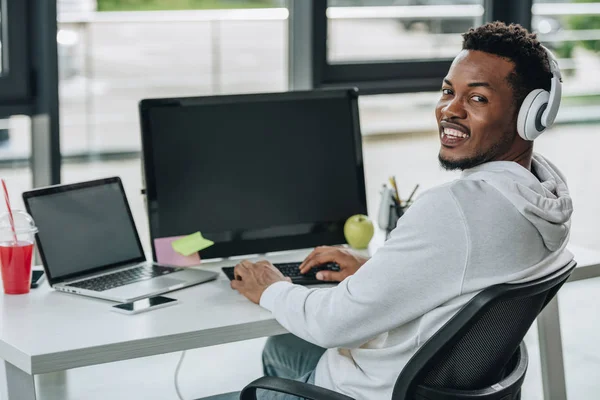 Programador americano africano alegre olhando para a câmera enquanto sentado no local de trabalho — Fotografia de Stock