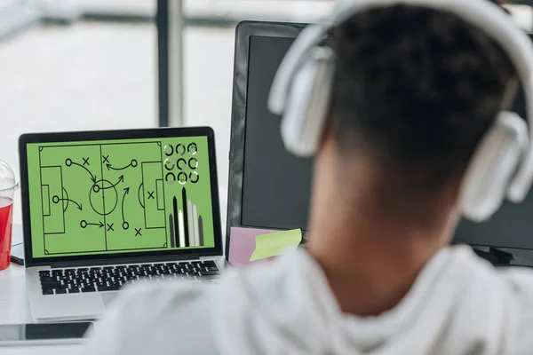 Back view of african american programmer in headphones playing football video game — Stock Photo