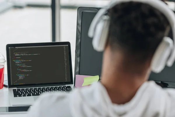 Visão traseira do programador americano africano nos fones de ouvido que trabalham no portátil no escritório — Fotografia de Stock