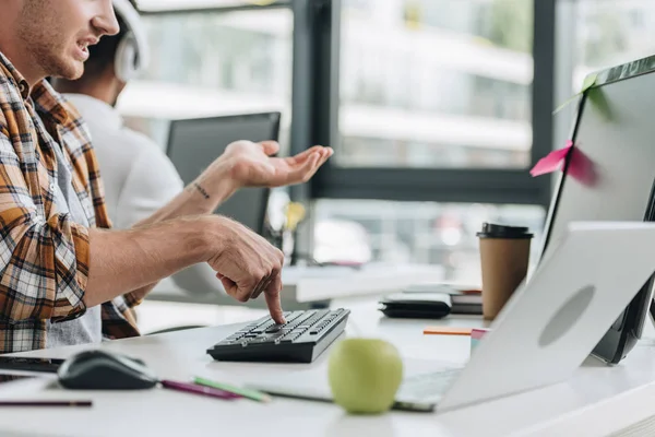 Vista recortada del gesto del programador mientras que trabaja en oficina cerca de colega afroamericano - foto de stock