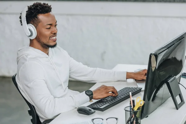 Heureux programmeur afro-américain assis sur le lieu de travail dans les écouteurs — Photo de stock