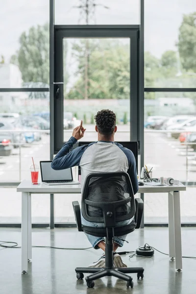 Visão traseira do programador americano africano novo que mostra o sinal da ideia ao sentar-se no local de trabalho no escritório — Fotografia de Stock