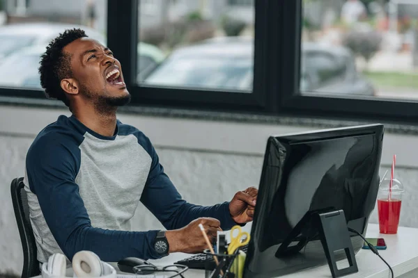Programmeur afro-américain en colère gestuelle tout en étant assis sur le lieu de travail dans le bureau — Photo de stock