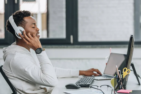 Jeune programmeur afro-américain dans les écouteurs travaillant sur ordinateur au bureau — Photo de stock