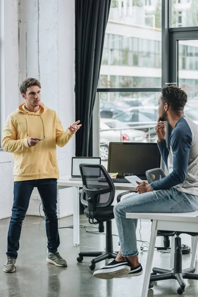 Dos programadores multiculturales discutiendo ideas en la oficina - foto de stock