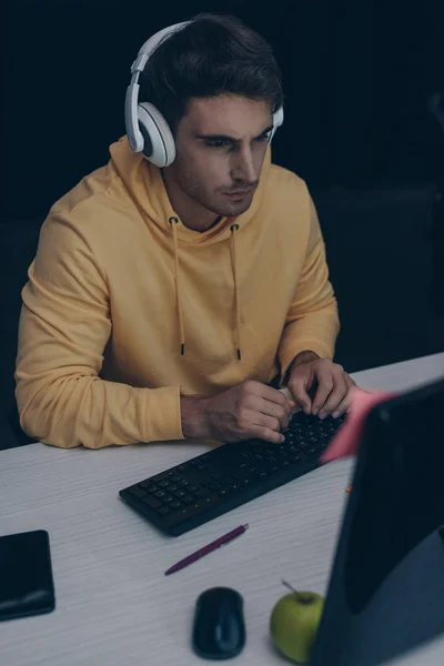 Joven programador en auriculares trabajando de noche en la oficina - foto de stock