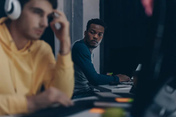 Selective focus of african american programmer looking at colleague in headphones — Stock Photo