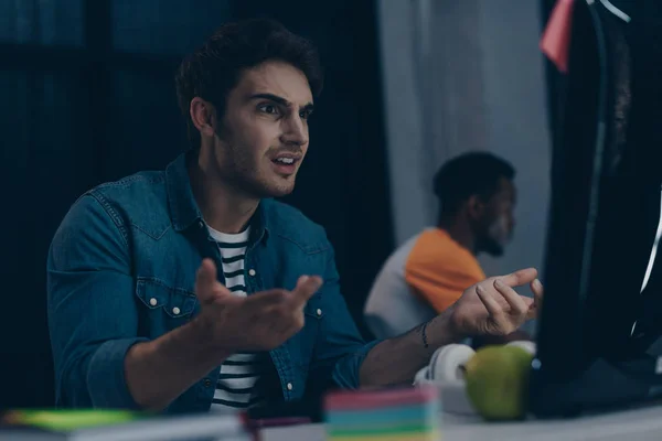 Shocked programmer gesturing while working near african american colleague at night in office — Stock Photo