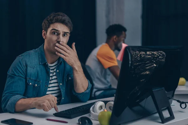 Foyer sélectif du programmeur choqué regardant la caméra tout en travaillant près d'un collègue afro-américain — Photo de stock