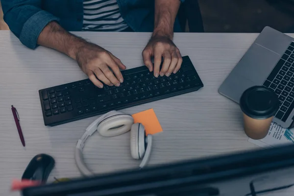 Vista recortada del programador escribiendo en el teclado por la noche en la oficina - foto de stock