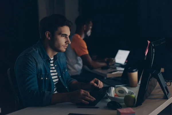 Selective focus of young programmer working at night near african american colleague — Stock Photo