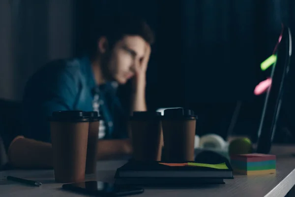 Selective focus of young programmer working at night near disposable cups — Stock Photo