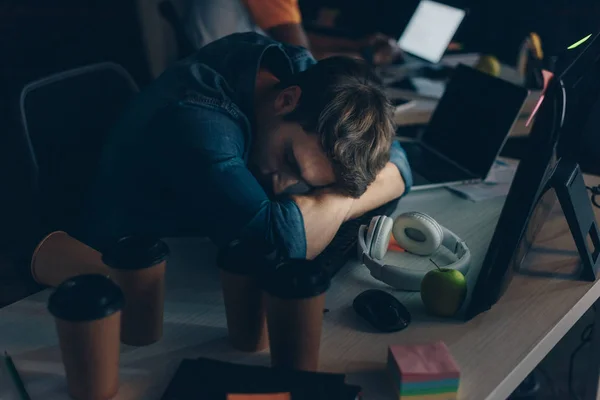 Junger, erschöpfter Programmierer schläft nachts am Arbeitsplatz im Büro — Stockfoto