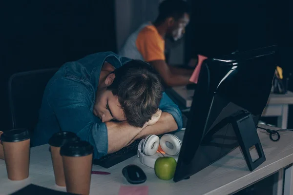 Focalizzazione selettiva del programmatore stanco che dorme sul posto di lavoro vicino al collega afroamericano — Foto stock