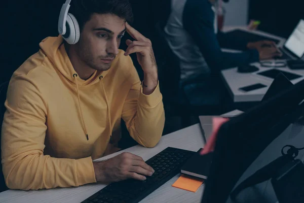 Enfoque selectivo de programador joven en auriculares que trabajan en la computadora cerca de colega afroamericano - foto de stock