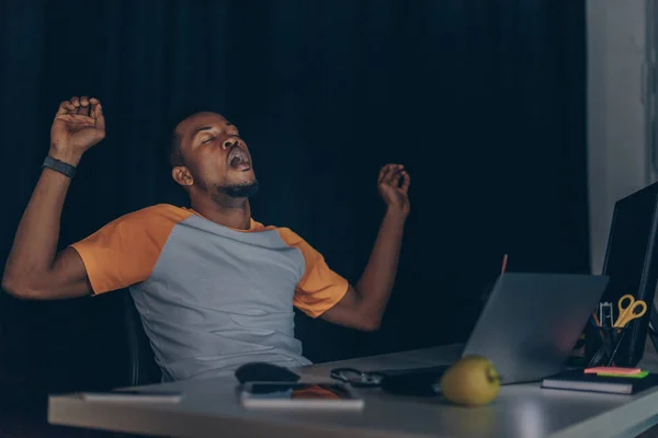 Programador afroamericano cansado bostezando mientras está sentado en la noche en la oficina - foto de stock