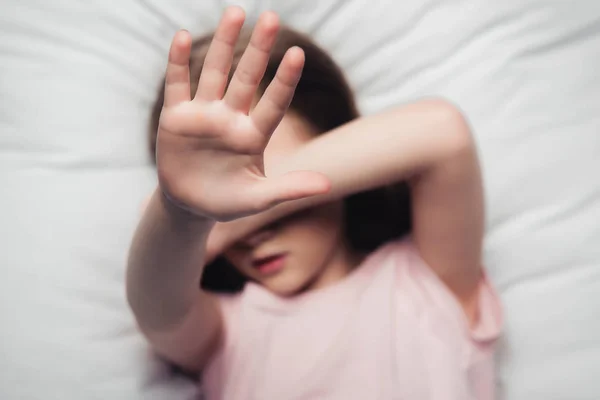 Bambino spaventato che copre il viso con la mano mentre sdraiato su biancheria da letto — Foto stock