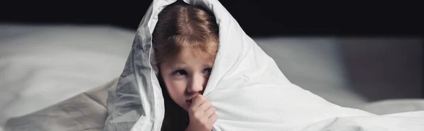 Panoramic shot of scared child hiding under blanket isolated on black — Stock Photo